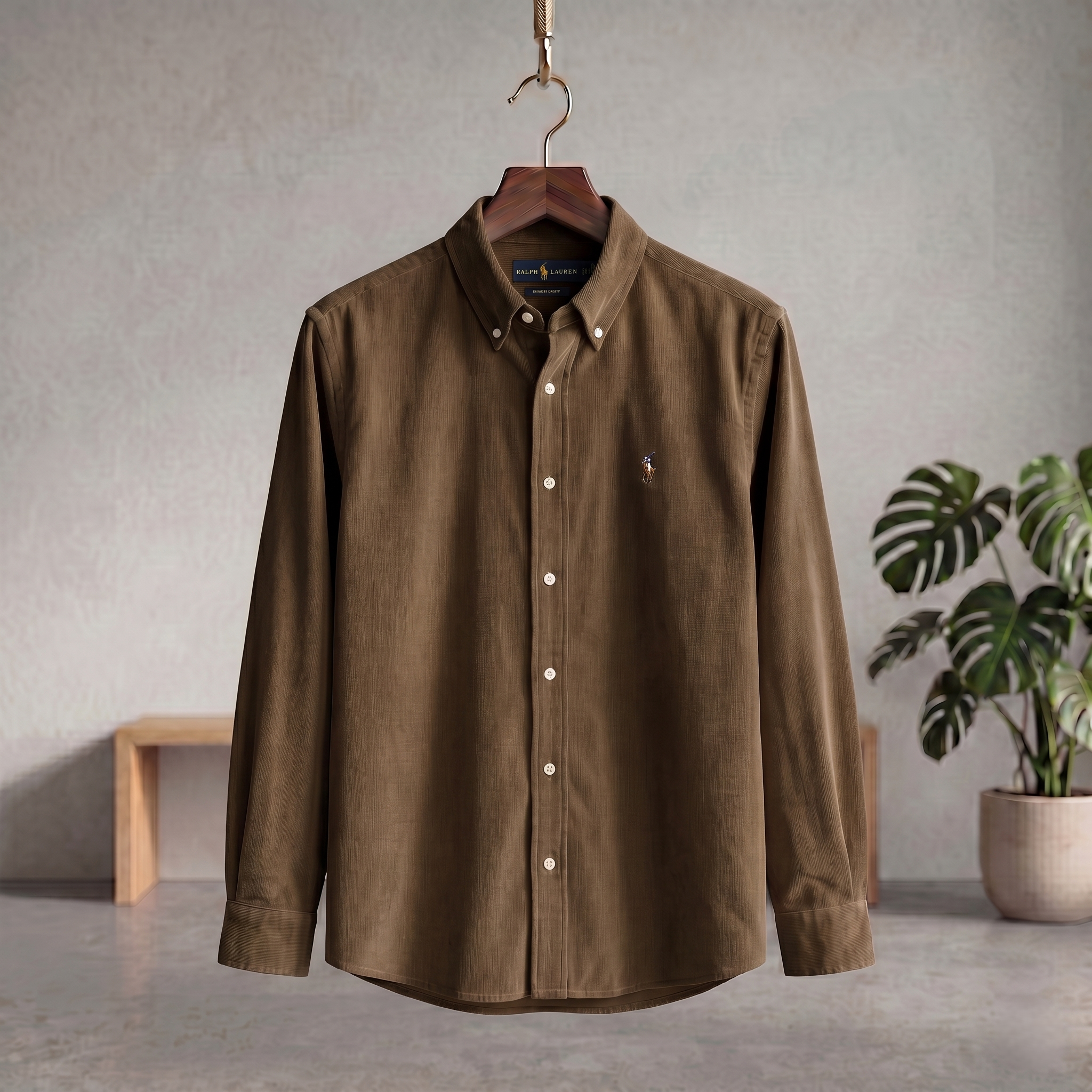 Brown corduroy button-up shirt with collar and long sleeves, hanging on a hanger.