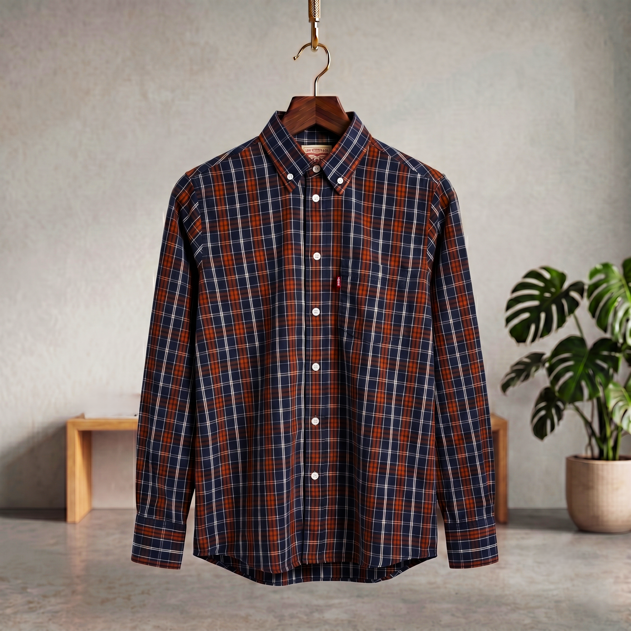 Navy & rust/brown Plaid shirt on a hanger against a neutral background with a plant.